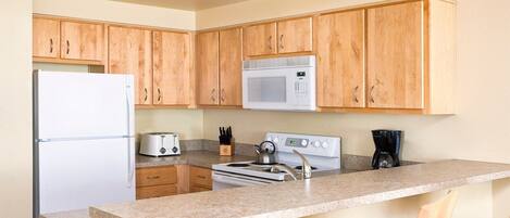 A kitchen with wooden cabinets, a white refrigerator, a microwave, a stove, and a coffee maker.