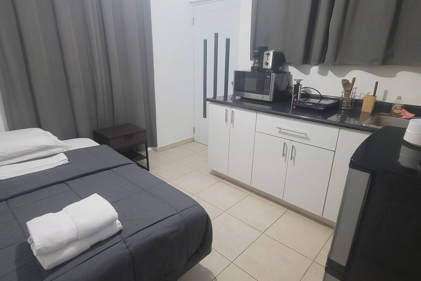 Hotellihuone, jossa on sänky, pieni pöytä, mikroaaltouuni ja kahvinkeitin.