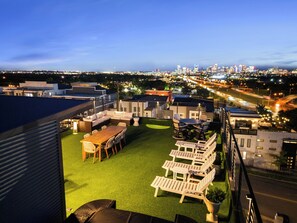 A rooftop terrace with outdoor furniture, a view of the city skyline, and a well-lit urban street.