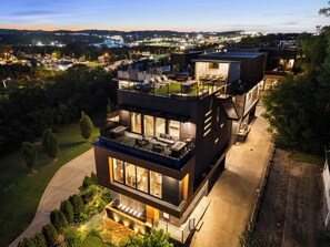A modern multi-story building with a rooftop terrace, large windows, and a well-maintained garden.
