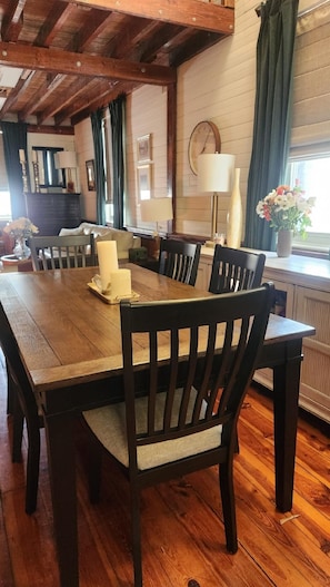 Un coin repas avec une table et des chaises en bois, une horloge au mur et une fenêtre avec des rideaux.