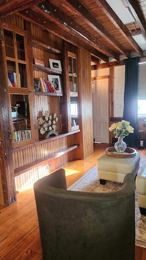 Une pièce chaleureuse aux murs en bois, avec une bibliothèque, un banc et une petite table sur laquelle est posé un vase.