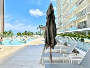Ein Hotelpoolbereich mit blauem Himmel, einem Pool, Liegestühlen und einem Gebäude mit Balkonen.