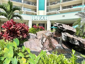 Ein Hotel mit Felswasserfall, üppiger Bepflanzung und einem mehrstöckigen Gebäude mit Balkonen.