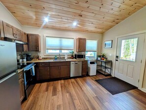 A kitchen with wooden cabinets, a stainless steel refrigerator, a microwave, and a dishwasher. - New Garden Retreat w/ Fire Pit, 5 Min to Town (Ellsworth)