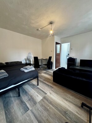 A modern bedroom with a bed, a desk, a chair, a sofa, and a ceiling fan. - Stylish Studio In Manchester City Centre - Sleeps 3 (Manchester)