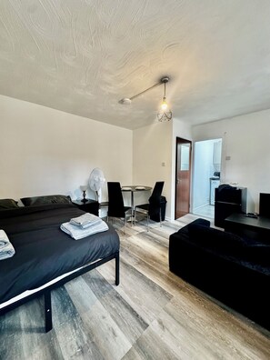 A modern hotel room with a bed, a small table with chairs, a kitchenette, and a door leading to another room. - Stylish Studio In Manchester City Centre - Sleeps 3 (Manchester)