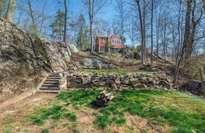 A rustic cabin with a stone staircase leading up to it, surrounded by trees and a grassy area. - Cozy Ranch Steps from the Lake. (Andover)