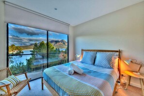 A bedroom with a large window, a bed, a chair, and a bedside table. - Furneaux - Complete Waterfront (Glamorgan-Spring Bay)
