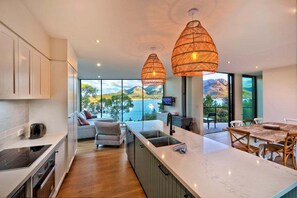 A modern kitchen with a large island, wooden flooring, and a view of the sea. - Furneaux - Complete Waterfront (Glamorgan-Spring Bay)