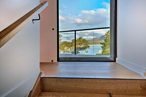 A modern interior with a wooden staircase leading to a balcony overlooking a scenic landscape. - Furneaux - Complete Waterfront (Glamorgan-Spring Bay)