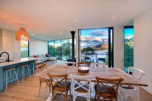 A modern kitchen with a bar area, large windows, and a dining table with chairs. - Furneaux - Complete Waterfront (Glamorgan-Spring Bay)