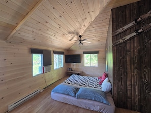 A wooden cabin bedroom with a bed, a ceiling fan, and a TV mounted on the wall.