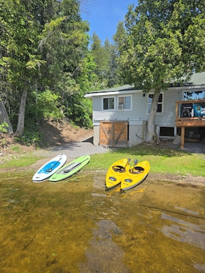 A lakeside cabin with kayaks, a covered deck, and a small shed.