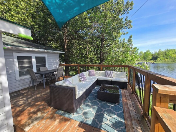 A covered deck with a sofa, a table, and chairs, overlooking a lake.