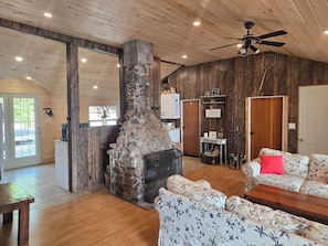 A rustic cabin interior with a stone fireplace, wooden walls, a ceiling fan, and a floral-patterned sofa.