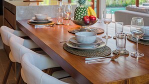 A dining table set with plates, bowls, and glasses, with a fruit bowl and a pineapple centerpiece. - Apura Panoramic Villa 2BD Ubud (Ubud)