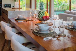 A dining table set with plates, bowls, and glasses, with a fruit bowl and a pineapple centerpiece. - Apura Panoramic Villa 2BD Ubud (Ubud)