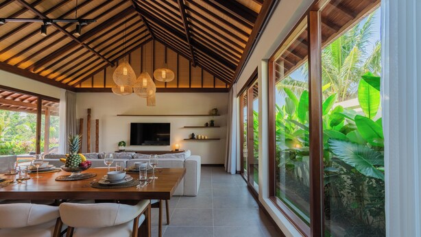A modern dining area with a wooden table set for a meal, a sofa, and a TV in the background. - Apura Panoramic Villa 2BD Ubud (Ubud)