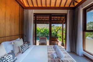 Quarto com cama, almofadas, janela e vista para uma piscina e vegetação.