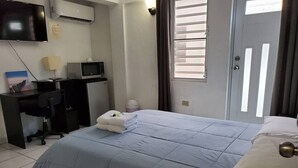 Een hotelkamer met een bed, een bureau met een computer, een televisie en een raam met jaloezieën.
