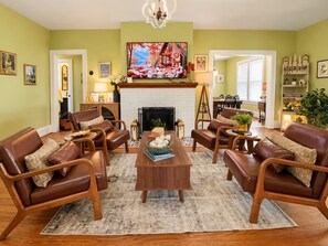 A living room with a fireplace, leather sofas, a coffee table, and a television mounted above the fireplace. - 1917 Bristol Tudor, Sleeps 10, Minutes to Downtown, BMS Speedway & Holston River (Bristol)