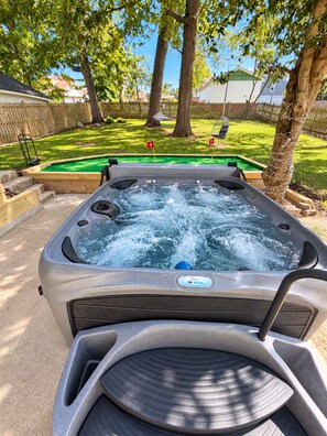 A hot tub with a control panel, surrounded by a wooden deck and a green lawn.