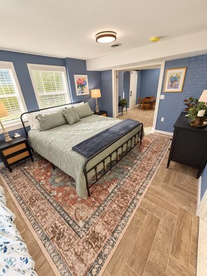 A bedroom with a bed, bedside tables, a nightstand, a bench, a rug, a door leading to a dining area, and a wall with a picture. - 1917 Bristol Tudor, Sleeps 10, Minutes to Downtown, BMS Speedway & Holston River (Bristol)