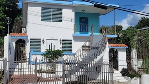A two-story building with a white facade, blue accents, a gated entrance, and a staircase leading to the upper level. - Above the Plaza 6 🏖 (with A/C) (Rincon)