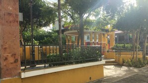 A yellow building with a white balcony, surrounded by trees and a paved walkway. - Above the Plaza 6 🏖 (with A/C) (Rincon)