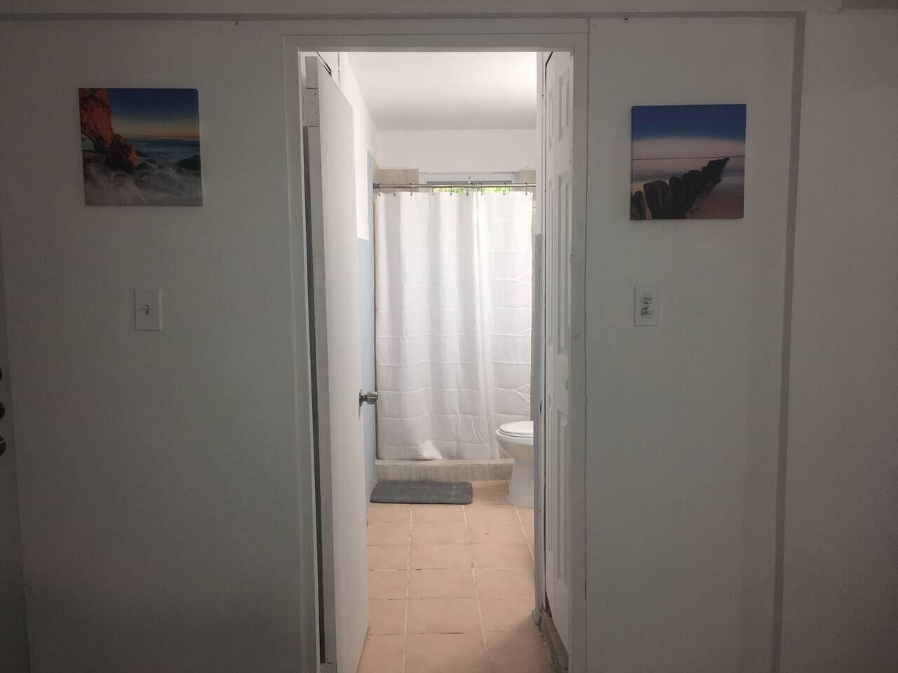 A hallway leading to a bathroom with a shower curtain, a toilet, and a small mat.