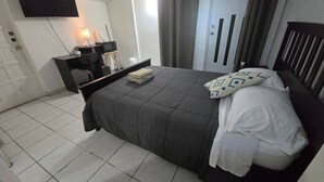 A bedroom with a bed, a desk, a chair, a TV, and a wardrobe. - Above the Plaza 6 🏖 (with A/C) (Rincon)