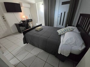 Ein Schlafzimmer mit Bett, Schreibtisch, Stuhl, Fernseher und Kleiderschrank.