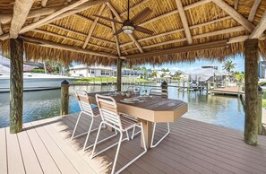 Ein überdachter Essbereich im Freien mit Tisch und Stühlen, einem Deckenventilator und Blick auf eine Marina mit Booten.