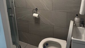 A bathroom with a toilet, a shower, and a towel hanging on the wall. - Tranquil Cabin Retreat in Bexleyheath (Bexleyheath)