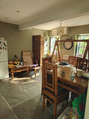 A dining area with a wooden table, chairs, a swing, and a refrigerator. - Cottage Sleeps 5 with Parking (Lydbrook)