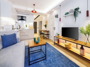 A modern living space with a sofa, coffee table, TV, kitchen, dining area, and a hallway leading to another room. - Cozy 2 Bedroom Apartment At Monnas Suite (Beyoglu)