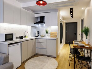 A modern kitchen with white cabinets, a microwave, a kettle, and a dining area with a table set for two. - Charming 2 Bedroom Apartment At Monnas Suite (Beyoglu)