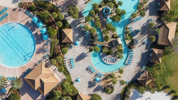 An aerial view of a resort with multiple swimming pools, lounge areas, and palm trees.