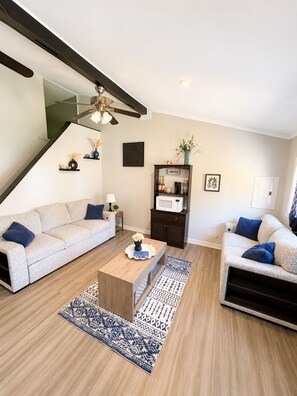 Ein Wohnzimmer mit zwei Sofas, einem Couchtisch, einer Kommode mit Kaffeeschild und einem Deckenventilator.