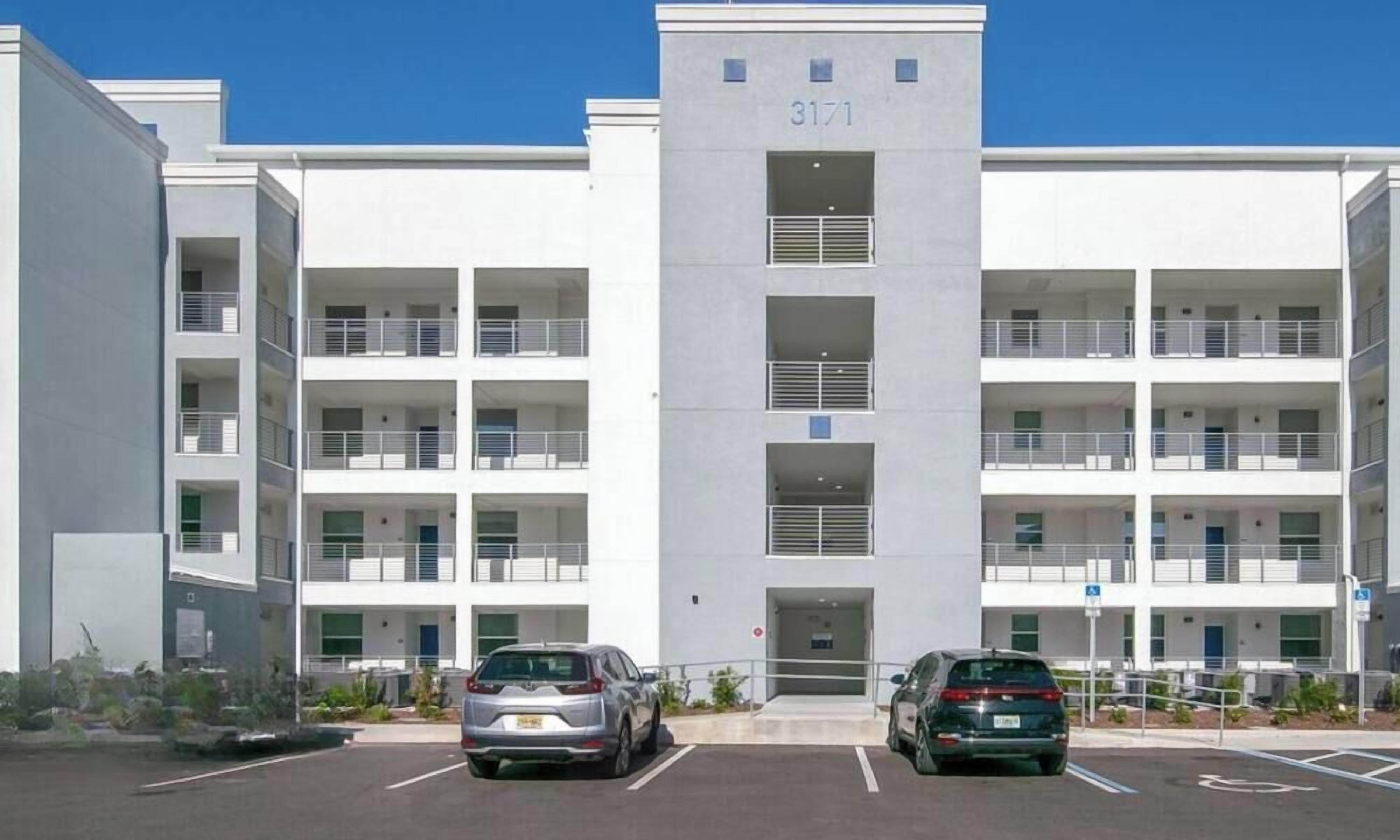 A multi-story building with balconies, a parking lot, and a clear sky.