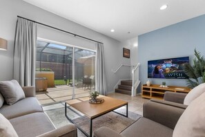 A modern living room with a sofa, coffee table, TV, and a staircase leading to a balcony. - 3063 Townhouse Hot Tub Resort Pools near Disney (Kissimmee)