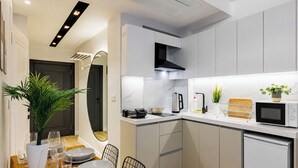 A modern kitchen with white cabinets, a microwave, a kettle, and a dining area with a table set for two. - Magical 2 Bedroom Apartment At Monnas Suite (Beyoglu)