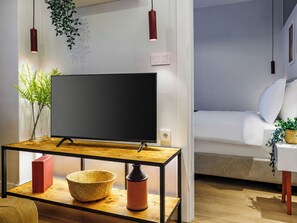 Ein modernes Wohnzimmer mit Fernseher auf einem Holztisch, einer Couch und einem kleinen Beistelltisch mit Pflanze.
