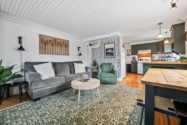 A living room with a grey sofa, a patterned rug, a wooden coffee table, and a green armchair. - Woodside Oasis | Walking distance to Downtown Rangeley (Rangeley)