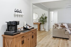 Moderni olohuone, jossa on kahvinkeitin, puinen kaappi, sohva, peili ja ruukkukasvi.
