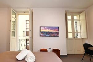 Una camera d'albergo con un letto, una TV a muro e vista sulla città.