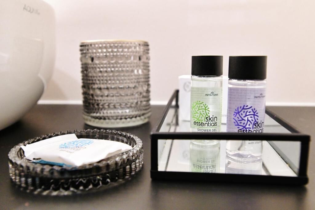 A bathroom counter with a glass tray holding a tissue, two bottles of shower gel, and a decorative glass container.