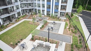 A multi-story building with outdoor seating areas, a barbecue setup, and a parking lot.