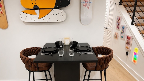 Une table à manger avec des chaises noires, une bougie et un skateboard accroché au mur, sur lequel on peut lire « ONCLE COCHON ».